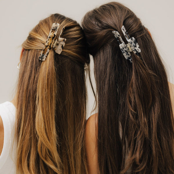 Zwei Frauen mit offenem Haar tragen unsere Haarklammern aus Bio-Acetat – links im Tortoise-Muster, rechts in Schwarz-Weiß. Die Köpfe sind aneinandergelehnt, aufgenommen von hinten.