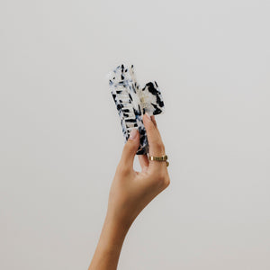 Hand hält unsere Tortoise-Haarklammer in schwarz-weiß aus Bio-Acetat in die Luft – Fokus auf Form, Muster und Qualität.
