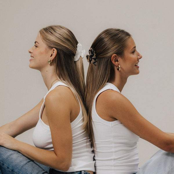 Zwei Frauen Rücken an Rücken: links mit unserem Scrunchie in Shell, rechts mit Tortoise – beide im halboffenen Look gestylt.