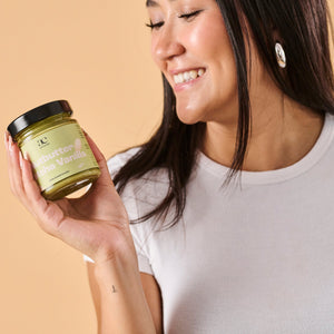 Frau betrachtet lächelnd ein Glas Nutbutter Matcha Vanilla von ae kitchen in ihrer Hand