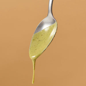 Nahaufnahme eines Löffels mit tropfender Nutbutter Matcha Vanilla von ae kitchen vor beigem Hintergrund