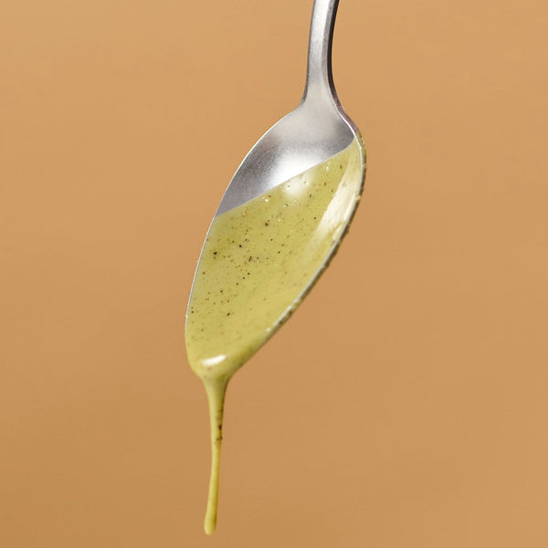 Nahaufnahme eines Löffels mit tropfender Nutbutter Matcha Vanilla von ae kitchen vor beigem Hintergrund