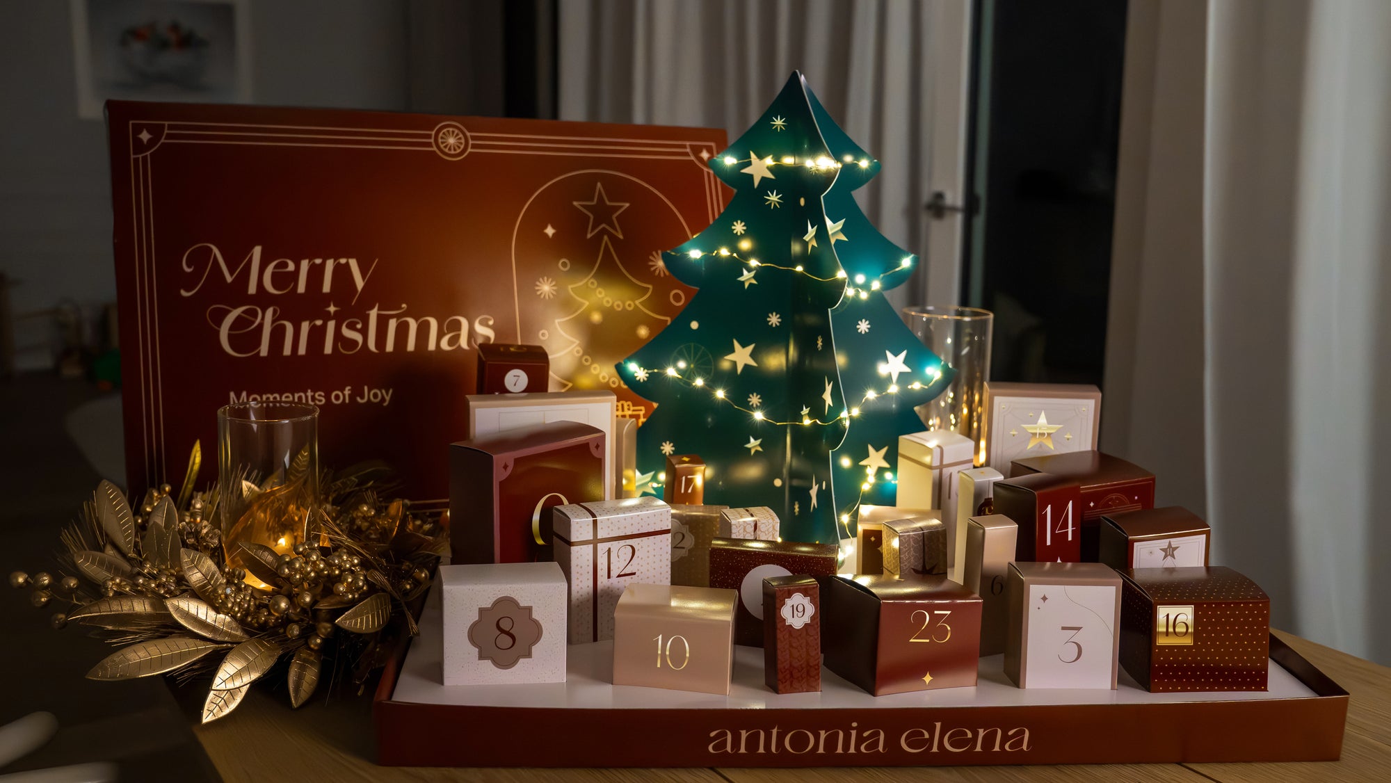 Adventskalender von Antonia Elena steht auf dem Tisch und man sieht alle Türchen mit dem Tannenbaum im Hintergrund mit Lichterkette.
