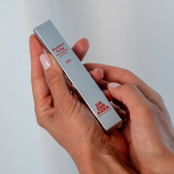 Zwei Hände die das Produkt von Dr. Emi den Lip Tint in der Hand hält.